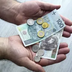 Dłonie trzymające polskie banknoty 100 zł i 10 zł oraz monety.